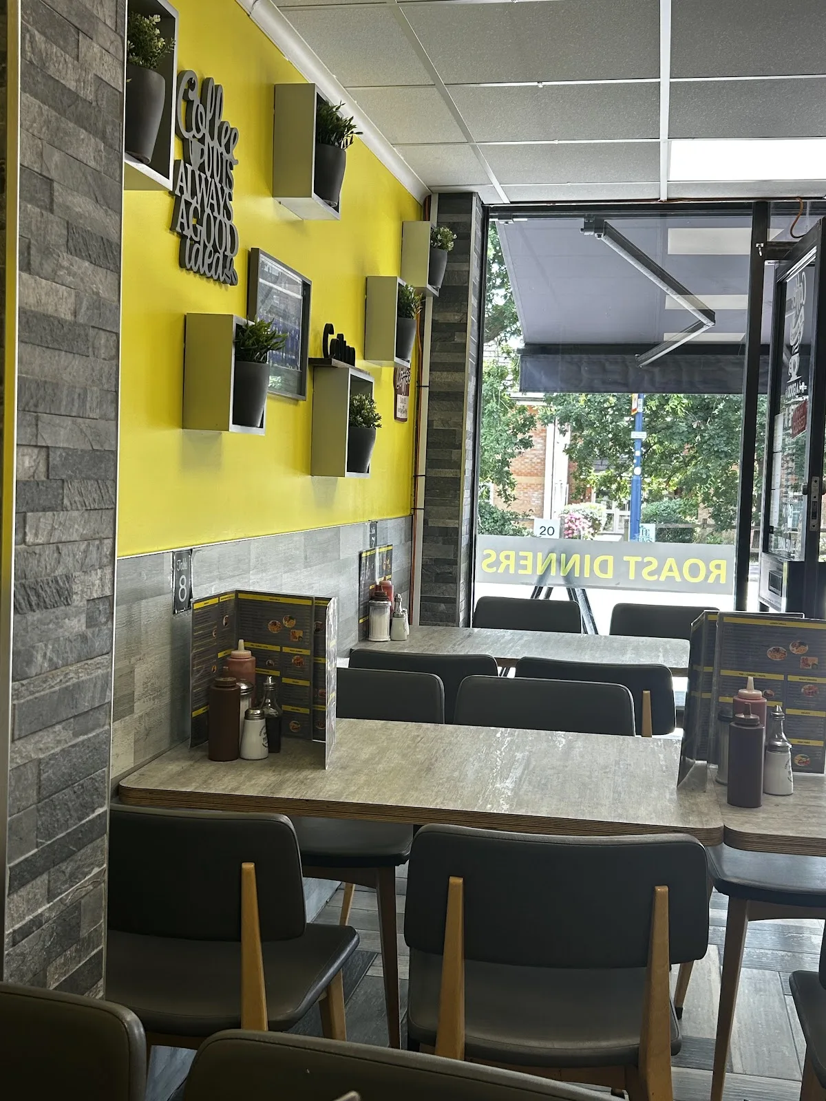 Inside Cowplain Cafe and Restaurant, yellow walls, grey tables and chairs and the sign reading coffee is always a good idea